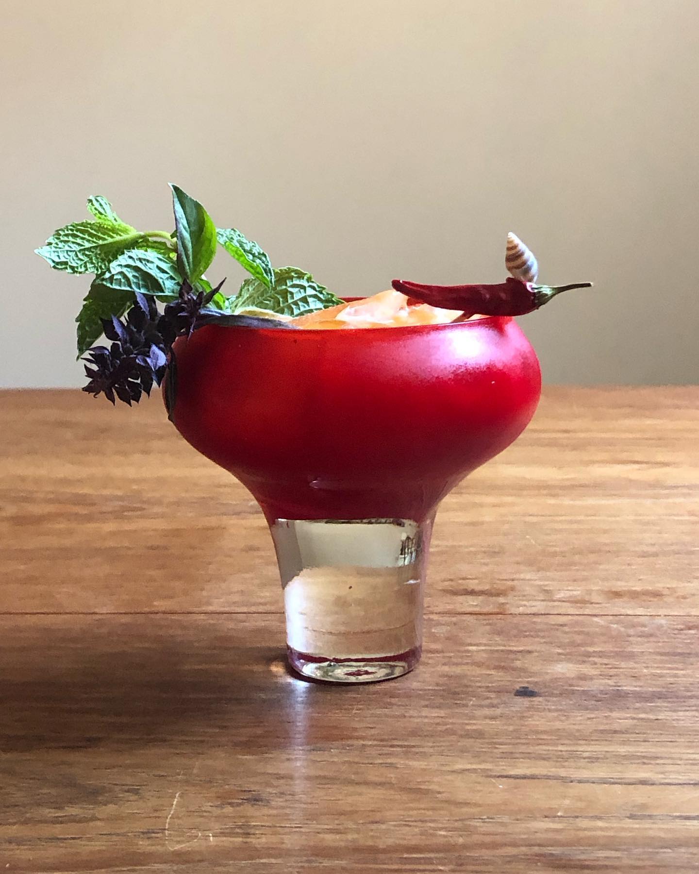 Red glass tiki cocktail with basil, mint, and chili